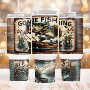May include: White stainless steel tumbler with a wood-grain design and a graphic of a fish with the text "Gone Fishing".