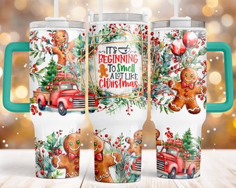 May include: A white tumbler with a teal handle features a watercolor design of gingerbread men, a red truck with a Christmas tree, and holly berries. The text "It's Beginning To Smell A Lot Like Christmas" is written in gold lettering on the tumbler.