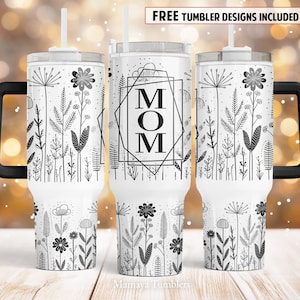 May include: White stainless steel tumbler with a black handle and lid. The tumbler features a black and white design of flowers and leaves with the word "MOM" in a geometric frame.