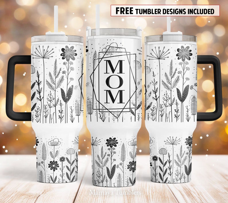 May include: White stainless steel tumbler with a black handle and lid. The tumbler features a black and white design of flowers and leaves with the word "MOM" in a geometric frame.