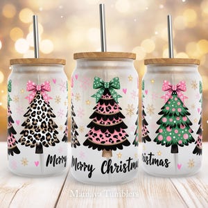 May include: Three glass tumblers with bamboo lids and stainless steel straws. Each tumbler features a Christmas tree design with a bow, snowflakes, and the words "Merry Christmas". The trees have leopard print, pink, and green accents.