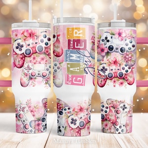 May include: A pink and white stainless steel tumbler with a pink handle. The tumbler features a floral design with a video game controller and the text "Gamer Girl" in pink and white letters.
