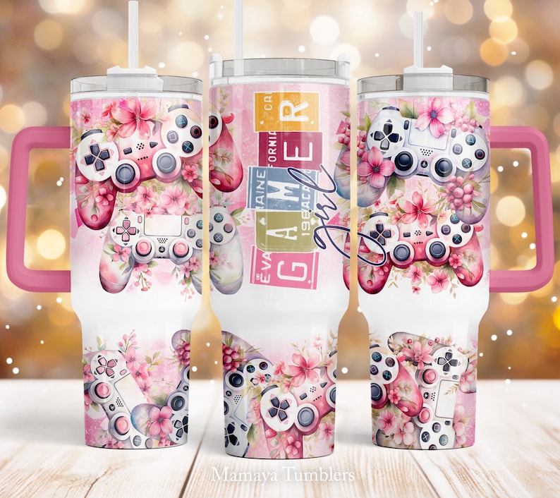 May include: A pink and white stainless steel tumbler with a pink handle. The tumbler features a floral design with a video game controller and the text "Gamer Girl" in pink and white letters.