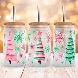 May include: Three frosted glass tumblers with wooden lids and metal straws. Each tumbler has a Christmas tree design in pink and green, surrounded by snowflakes. The text "Mamaya Tumblers" is at the bottom.
