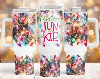 May include: White tumbler with a handle and a lid, featuring a colorful design of Christmas lights. The text "Christmas Junkie" is displayed in pink and green. The tumbler has a straw.