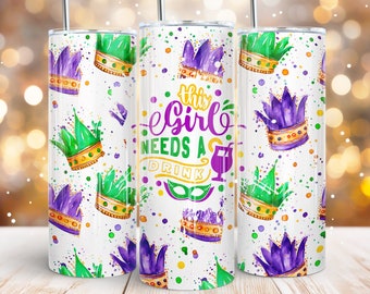 May include: A white tumbler with a purple, green, and gold Mardi Gras themed design. The tumbler has the text "This Girl Needs A Drink" with a martini glass icon.