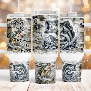 May include: A white tumbler with a camouflage pattern and a graphic of a fish jumping out of the water. The tumbler has a lid and a straw. The text "Born to Fish Forced to Work" is printed on the tumbler.