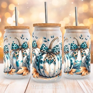 Op de afbeelding: Drie witte bekers met een ontwerp van een teal, zwart en bruin luipaardprint-pompoen. Elke beker heeft een rietje en een houten deksel.