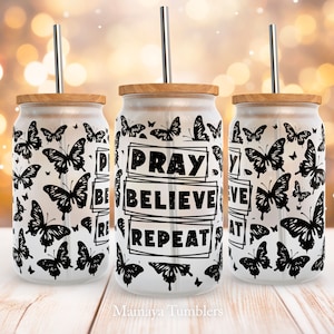 以下が含まれることがあります： 黒い蝶の模様と「祈る 信じる 繰り返す」という文字が書かれた、白いステンレス製のタンブラーが3つ。各タンブラーには木製の蓋とステンレス製のストローが付いています。