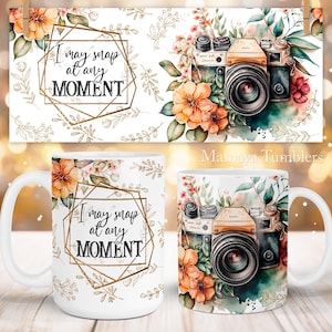 Może przedstawiać: Biały kubek ceramiczny z pozłacanym geometrycznym ramieniem i tekstem "I may snap at any MOMENT". Kubek ma akwarelowy wzór kwiatów i vintage'owego aparatu.