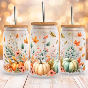 Può includere: Tre bicchieri di vetro trasparente con coperchi e cannucce. Ogni bicchiere presenta un diverso design a tema autunnale con zucche, foglie e fiori. I bicchieri sono etichettati "Mamaya Tumblers".