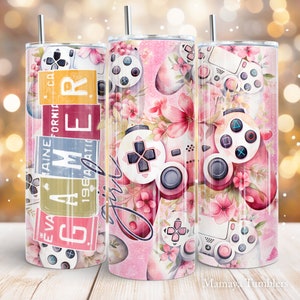 May include: Three pink and white stainless steel tumblers with a floral and video game controller design. The tumblers have a pink background with white flowers and a white video game controller with pink buttons. The text "Girl" is written on the tumbler in the centre.