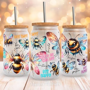 Peut inclure: Trois gobelets blancs avec un couvercle en bois et une paille. Chaque gobelet présente un motif d'abeille différent avec des ailes colorées et un fond de galaxie. Les gobelets ont des citations inspirantes sur les abeilles, telles que "Bee Sweet", "Bee Cool", "Cute as can Bee", "Bee Strong", "Bee Happy", "Bee Free", "Bee Different", "Bee Positive", et "Bee Humble".