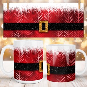 May include: Two white ceramic mugs with a red and white Santa Claus design. The mugs have a black belt with a gold buckle. The text "Mamaya Tumblers" is visible in the background.