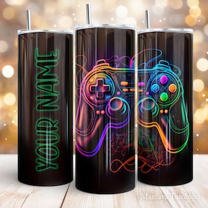 May include: Three stainless steel tumblers with a black background. The center tumbler features a neon rainbow colored video game controller with a black background. The tumbler on the left has the text "YOUR NAME" in green neon lettering.