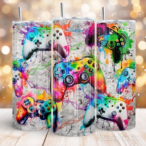 May include: Three stainless steel tumblers featuring a colourful video game controller design. The controllers are painted in vibrant rainbow hues and white, with paint splatter effects against a grey background. The tumblers have a straw.