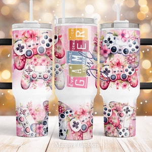 May include: A white stainless steel tumbler with a black handle and a pink and white floral design featuring a video game controller. The text "Gamer Girl" is printed on the side of the tumbler.