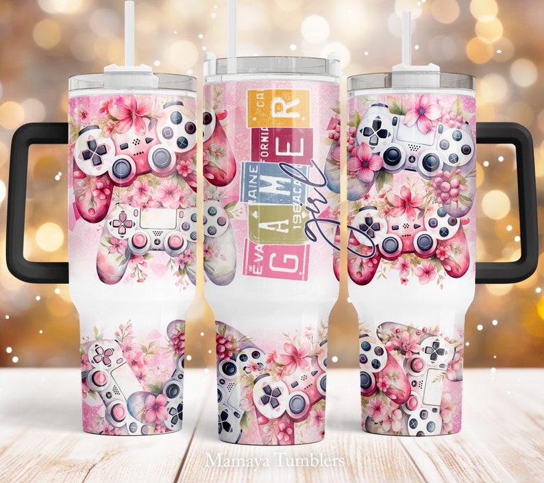 May include: A white stainless steel tumbler with a black handle and a pink and white floral design featuring a video game controller. The text "Gamer Girl" is printed on the side of the tumbler.