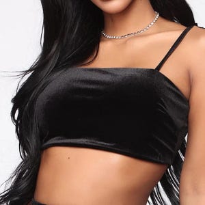 Puede incluir: Un top corto de terciopelo negro con tirantes finos ajustables. El top tiene un escote cuadrado y una silueta ajustada.