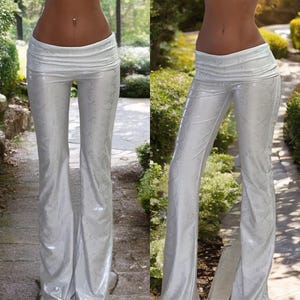 Puede incluir: Pantalones blancos acampanados con un patrón sutil y texturizado. Los pantalones tienen una cintura ancha y una silueta fluida, adecuados para ocasiones informales o elegantes. La tela parece tener un ligero brillo.