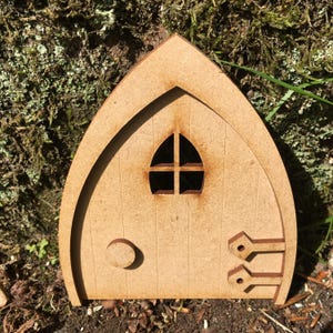 May include: A wooden fairy door with an arched top and a small window. The door has a round handle and decorative hinges. The door is made of light brown wood and is designed to be placed outdoors.
