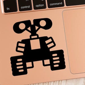 May include: A black vinyl sticker of the animated robot Wall-E, placed on a rose gold laptop. The sticker features Wall-E's distinctive design, including his boxy body, treads, and expressive eyes.