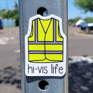 May include: A yellow and black safety vest sticker with the text "hi-vis life" on a metal pole.
