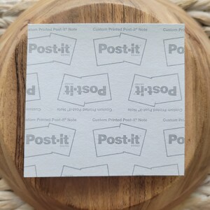Op de afbeelding: Een wit vel papier met een herhalend patroon van het Post-it-merklogo. Het logo is in grijs gedrukt en zegt "Post-it Brand" in een wit rechthoek. De tekst "Custom Printed Post-it Note" is in grijs gedrukt bovenaan en onderaan het vel.