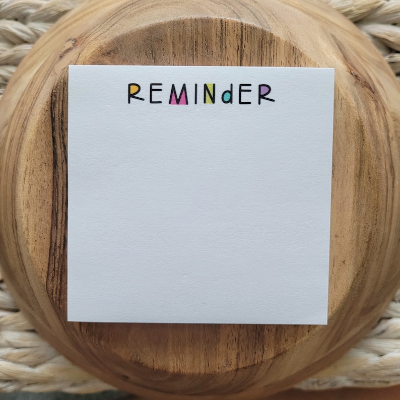 Op de afbeelding: Witte reminder notitieblok met het woord "REMINDER" in kleurrijke letters.