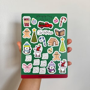 May include: A green sticker sheet featuring Christmas-themed illustrations. Designs include a coffee cup, ornaments, a red truck, gingerbread men, Christmas trees, candy canes, penguins, gnomes, and the word "Christmas". The sheet also has calendar dates.