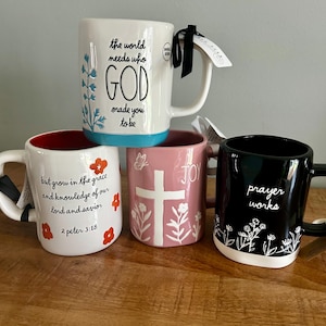May include: Four ceramic mugs with handles. One white mug features blue text and floral art. One white mug has red flowers and black text reading 2 peter 3:18. One pink mug displays a white cross and the word JOY. One black mug features white floral art and the text prayer works.