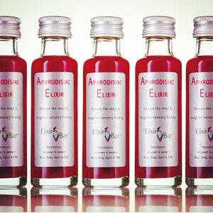 May include: Five small glass bottles with silver lids filled with a red liquid. Each bottle has a white label with the text "Aphrodisiac Elixir" and "Elixir Bar" with a small rainbow logo. The text on the label reads "Elevate the mind & heighten sensory feeling. Neurotonics empower & awaken Mind, Body, Spirit & DNA."