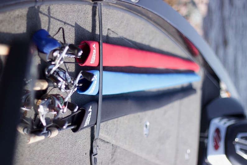 May include: Three fishing rods are stored in a boat, each with a protective sleeve. The sleeves are black, blue, and red, and each has the word "Y-TIGER" printed on it.