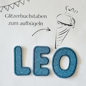 Könnte beinhalten: Blaue Glitzerbuchstaben mit der Aufschrift "LEO" mit dunkelblauem Rand. Die Buchstaben befinden sich auf weißem Hintergrund mit dem deutschen Text "Glitzerbuchstaben zum aufbügeln" und einer Strichzeichnung einer Schultüte.