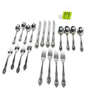 May include: A collection of ornate silverware, including forks, spoons, and knives, arranged on a white surface. The silverware features a detailed floral pattern on the handles. The image includes the text "MY" on a green tag.