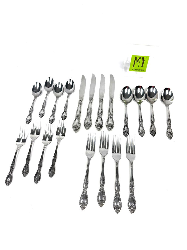May include: A collection of ornate silverware, including forks, spoons, and knives, arranged on a white surface. The silverware features a detailed floral pattern on the handles. The image includes the text "MY" on a green tag.