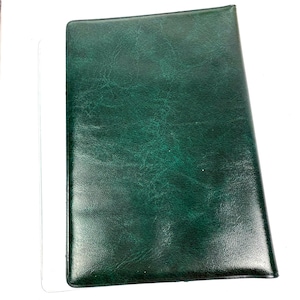 Peut inclure: Un journal ou un carnet de notes en cuir vert fonc&eacute;. La couverture pr&eacute;sente un aspect textur&eacute; et mouchet&eacute;. La forme rectangulaire est l&eacute;g&egrave;rement inclin&eacute;e, sugg&eacute;rant qu'il est pos&eacute; sur une surface. L'esth&eacute;tique g&eacute;n&eacute;rale est classique et professionnelle.