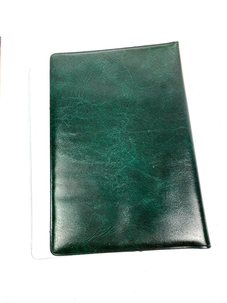 Peut inclure: Un journal ou un carnet de notes en cuir vert fonc&eacute;. La couverture pr&eacute;sente un aspect textur&eacute; et mouchet&eacute;. La forme rectangulaire est l&eacute;g&egrave;rement inclin&eacute;e, sugg&eacute;rant qu'il est pos&eacute; sur une surface. L'esth&eacute;tique g&eacute;n&eacute;rale est classique et professionnelle.