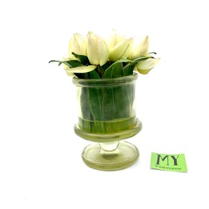 May include: A bouquet of white tulips in a clear glass vase with a pedestal base. The vase has a textured surface and is decorated with a green label that reads "MY 10 YEAR COLLECTION".