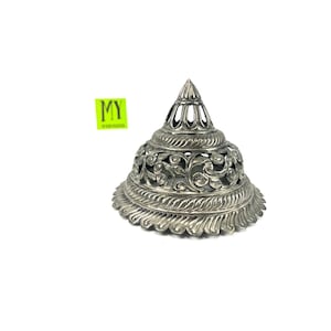 Peut inclure: Un couvercle décoratif en argent, orné de motifs découpés complexes. Le couvercle a la forme d'un cône avec une base arrondie.