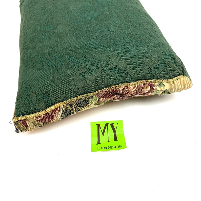 May include: A green pillow with a floral pattern on the border. The pillow has a textured surface and is made of a soft fabric. The pillow is labeled "MY 40 YEAR COLLECTION".