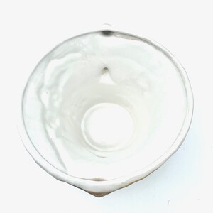 May include: A white ceramic bowl with a rounded shape and a small spout. The bowl has a smooth, glossy interior and a slightly textured exterior. The bowl is empty and appears to be clean.