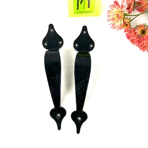 May include: Two black metal door handles with a pointed top and bottom. The handles have a simple design and are suitable for a variety of doors.