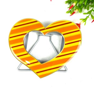 May include: A heart-shaped picture frame with a yellow and orange striped design. The frame is made of metal and has a stand.