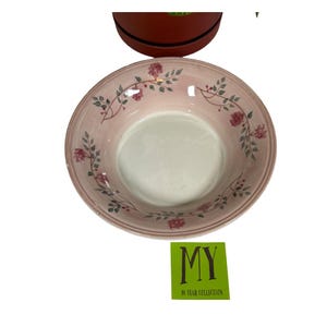 May include: A pink ceramic bowl with a white interior and a floral design. The bowl has a wide rim and is decorated with red flowers and green leaves. The text "MY 40 YEAR COLLECTION" is on a green sticker.