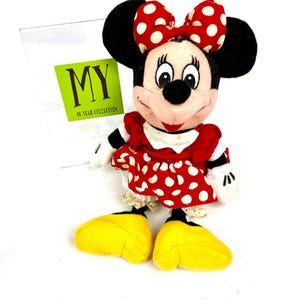 Vintage Minnie Mouse plush doll wearing a red polka dot dress and bow, displayed upright on a white background