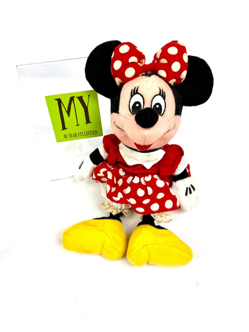 Vintage Minnie Mouse plush doll wearing a red polka dot dress and bow, displayed upright on a white background