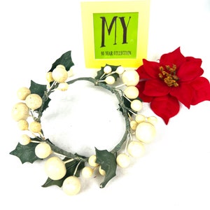 May include: A white and green Christmas wreath with white berries and green holly leaves. The wreath is on a white background with a yellow sign that says "MY 40 YEAR COLLECTION".