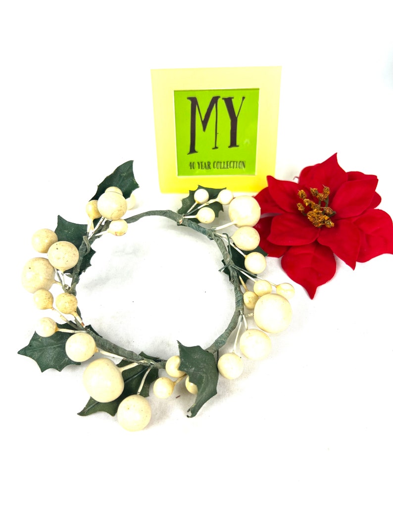 May include: A white and green Christmas wreath with white berries and green holly leaves. The wreath is on a white background with a yellow sign that says "MY 40 YEAR COLLECTION".