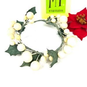 May include: A white and green artificial wreath with white berries and green leaves. The wreath is on a white background.
